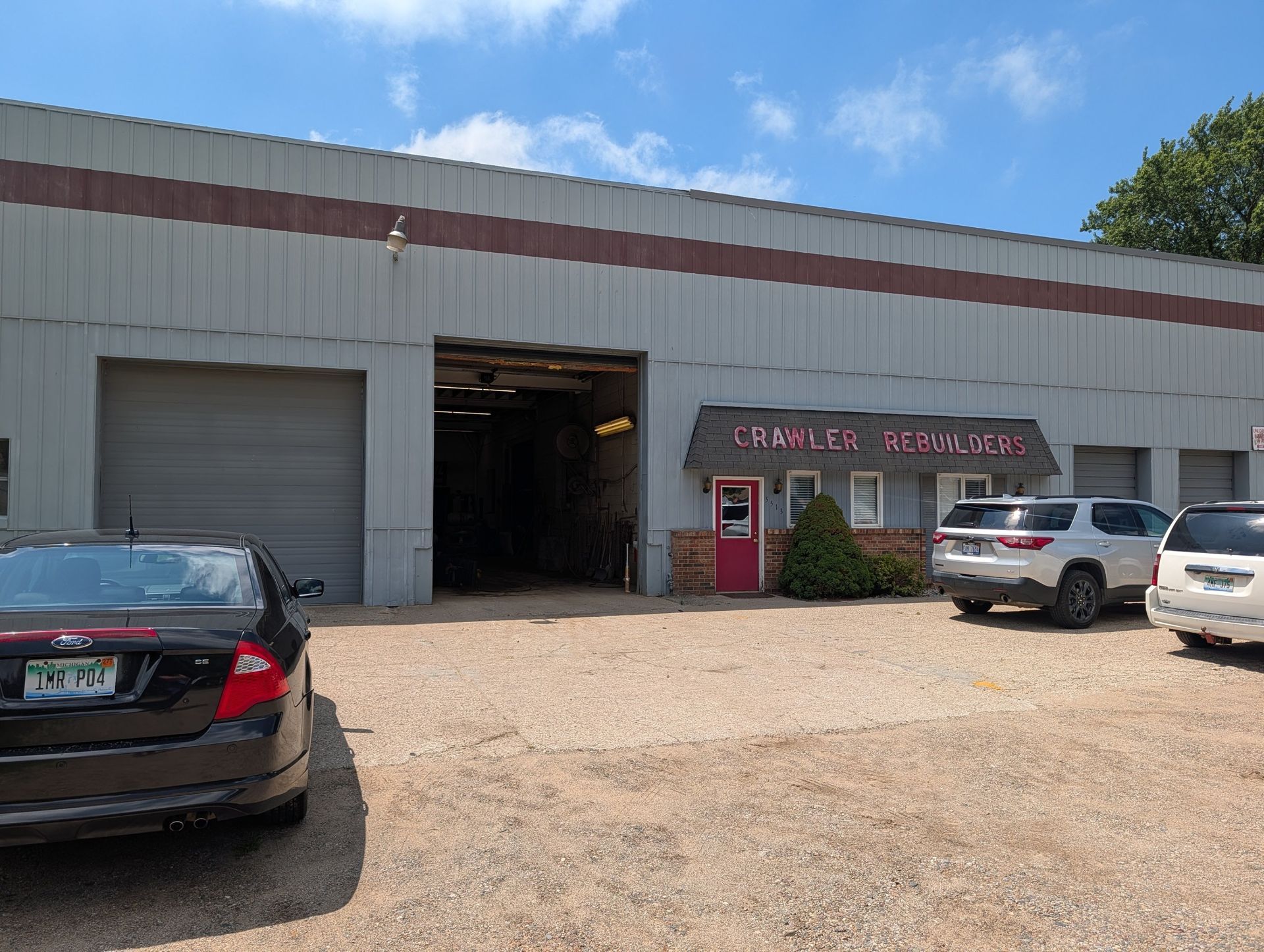 Auto repair shop with open bays and parked cars in a gravel lot under a blue sky