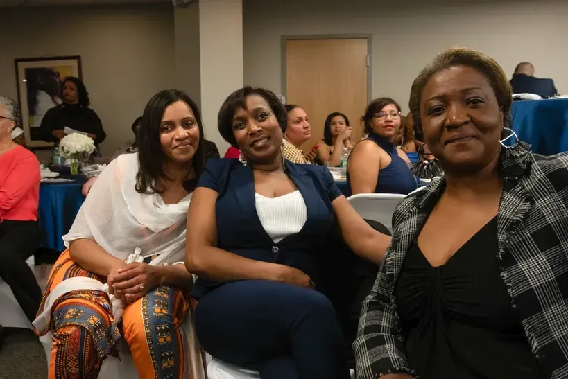 Three women are posing for a picture while sitting in chairs in a room.