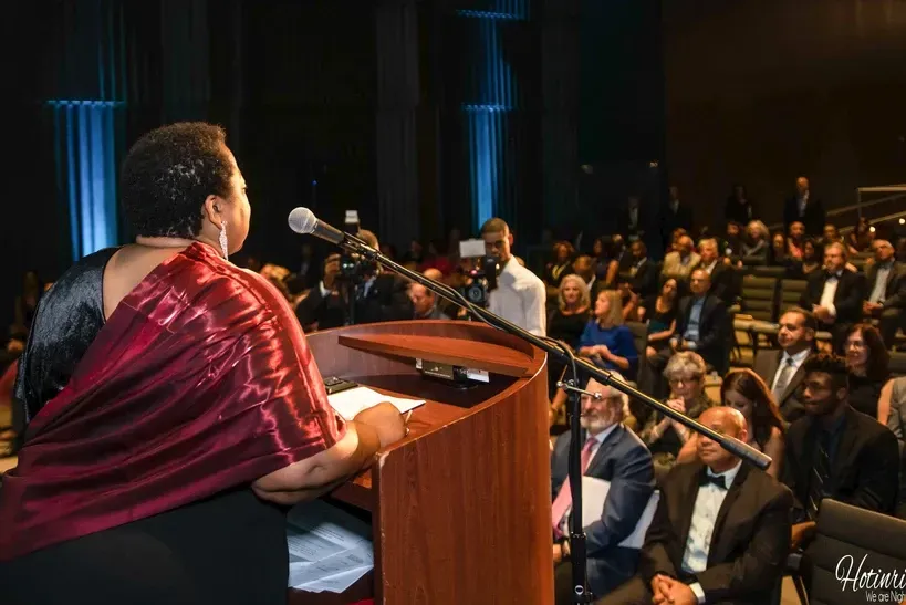 A woman is giving a speech at a podium in front of a crowd.