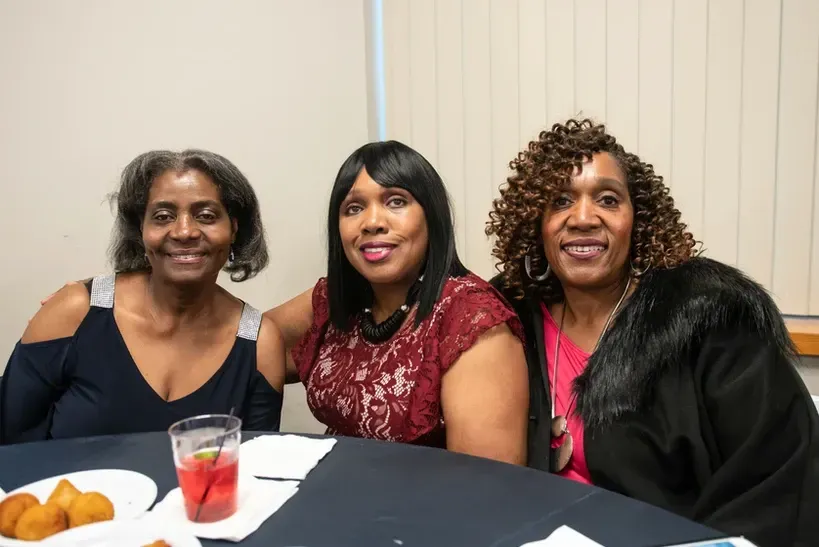 Three women are posing for a picture while sitting at a table.