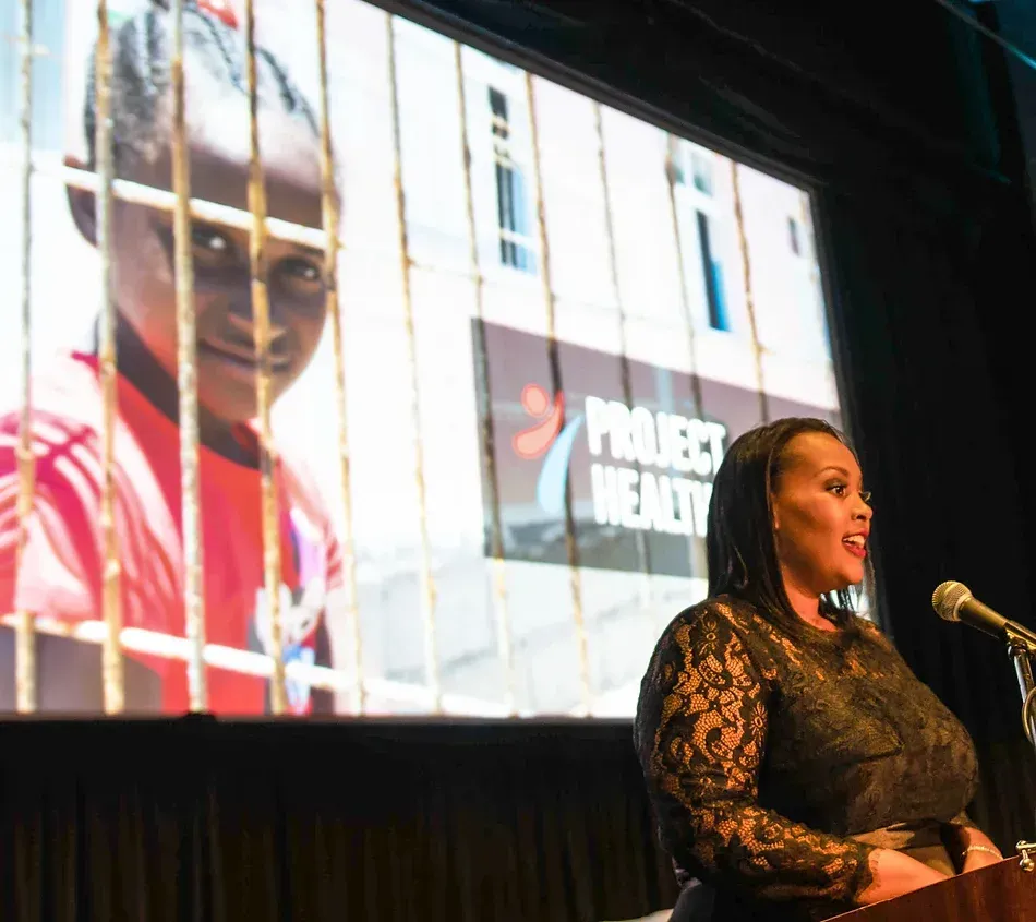 A woman stands at a podium in front of a project wendy screen