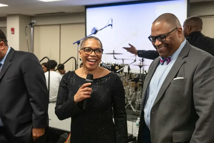 A woman is holding a microphone while standing next to a man in a suit.