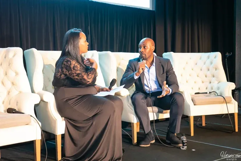 A man and a woman are sitting in chairs talking into microphones.