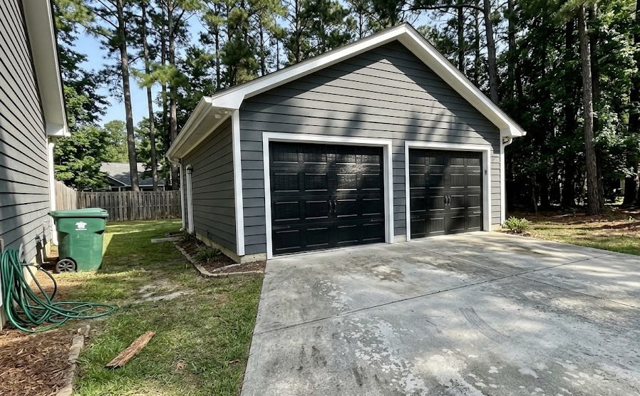 A newly constructed two-car detached garage with grey siding and black carriage doors built by Spokane General Contractor.
