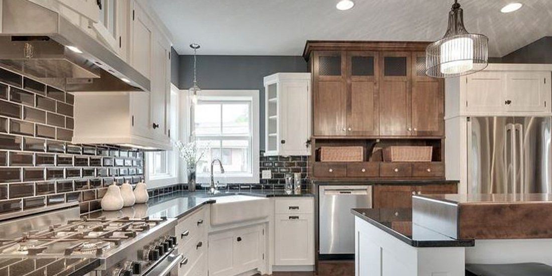Modern kitchen countertop in Spokane with white and wood cabinets, a farmhouse sink, stainless steel appliances, and dark tiled backsplash.