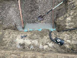 Trenching work around a buried pipe with tools and exposed dirt at the edge of a concrete area