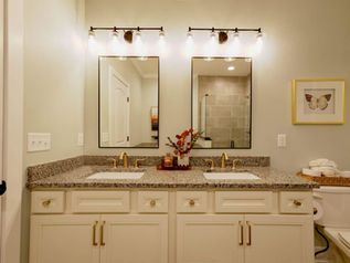 Bathroom vanity with double sinks, mirrors, granite countertop, and warm wall lights