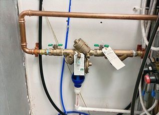 Copper plumbing with a valve assembly and blue filter in a utility room