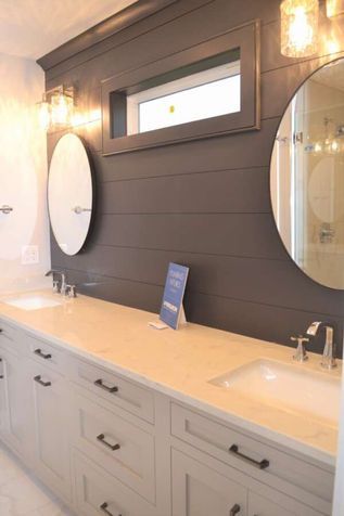 Modern bathroom vanity with double sinks, oval mirrors, and warm wall sconces on a dark accent wall