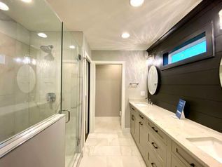 Modern bathroom with glass shower, long vanity, and dark accent wall under skylight.