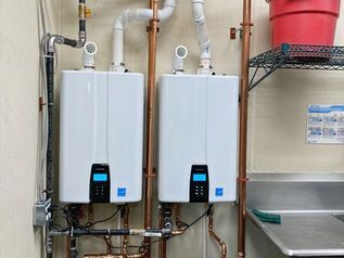 Two white tankless water heaters mounted on a wall in a utility room