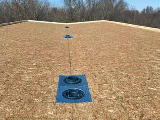 Rooftop with blue roof vents aligned along the center on plywood sheathing under a cloudy sky