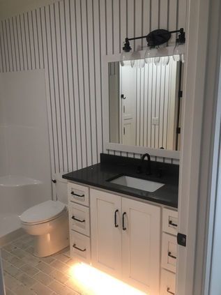 Bathroom vanity with black countertop, white cabinets, round sink, mirror, and toilet visible on the left
