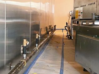 Metal processing room with large stainless tanks and industrial equipment along a narrow walkway