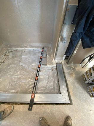 Empty elevator shaft with a metal measuring pole on the floor and a person standing at the right edge.