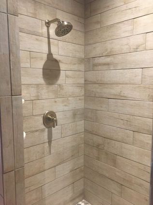 Stone-tiled shower corner with rainfall showerhead and wall-mounted control.