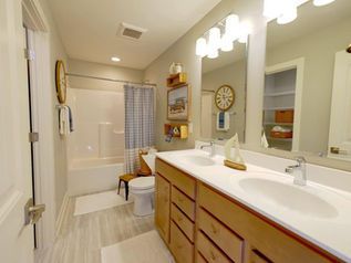 Bright bathroom with double vanity, large mirror, tub-shower, and light beige walls
