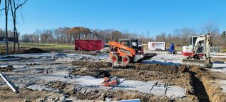 Construction site with excavator, skid steer, and workers on muddy ground under a clear sky