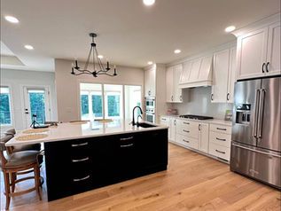 Modern white kitchen with black island, stainless steel appliances, and hardwood floors