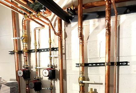 Basement wall with copper pipes, valves, and two circulating pumps for plumbing or heating system