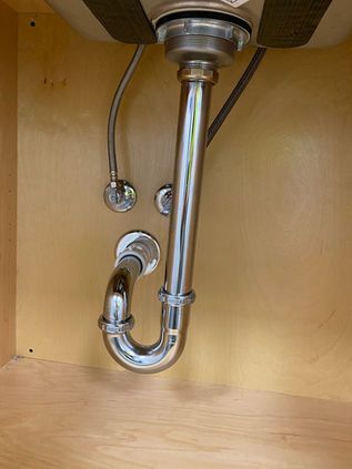 Under-sink chrome plumbing with P-trap and drain pipes inside a wooden cabinet