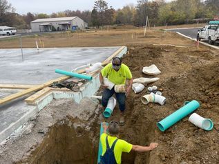Workers installing turquoise drainage pipes at a roadside construction site.