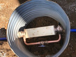 Coiled gray hose with a small valve and metal pipe assembly lying on dirt.