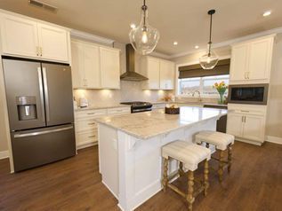 Modern kitchen with white cabinets, stainless fridge, island, and two stools by a window.