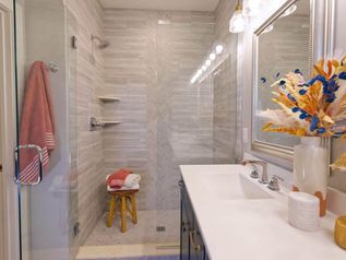 Bright bathroom with glass shower, white vanity, pink towel, and flowers on the counter.