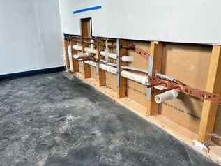 Exposed plumbing and open wall framing in a room with unfinished concrete floor