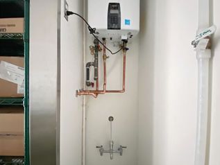 Boiler and exposed copper pipes mounted on a white utility room wall with a tap below