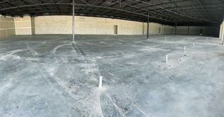 Empty concrete warehouse floor with white markings under a large metal roof