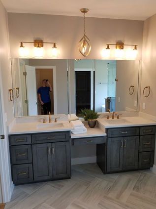 Double vanity bathroom with gray cabinets, large mirror, and warm wall lights