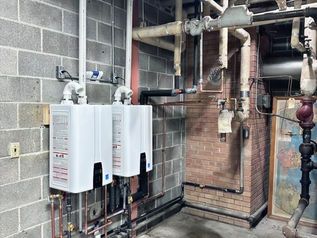 Wall-mounted boilers and exposed pipes in an industrial utility room.