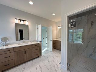 Modern bathroom with double vanity, large mirror, glass shower, and marble tile flooring.