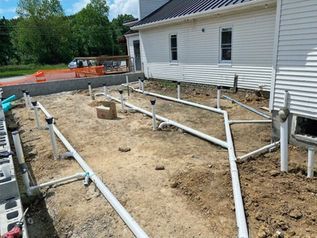 Accessible ramp construction beside a white house, with white railings over a dirt foundation area