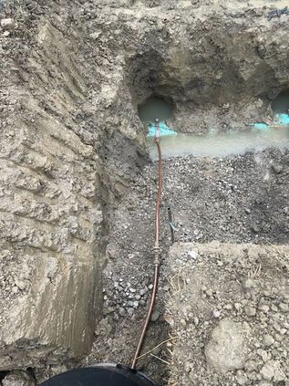 Excavation trench with rough soil walls and a pipe running down the center, with water pooling near the top.
