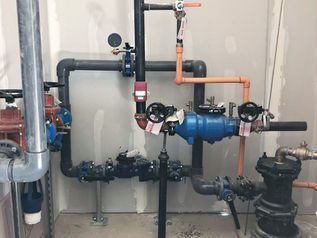 Industrial plumbing pipes and valves in a utility room, with blue and black pipe fittings mounted on a wall.