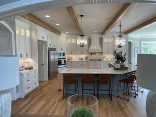 Bright white kitchen with island, wood beams, pendant lights, and barstools in a modern home