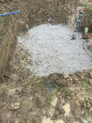 Fresh gray gravel poured into an outdoor excavation beside dirt walls and exposed pipes