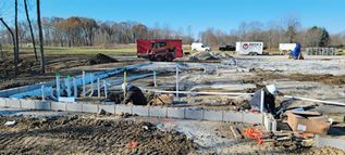 Construction site with foundation forms, rebar, workers, and trucks under a clear blue sky