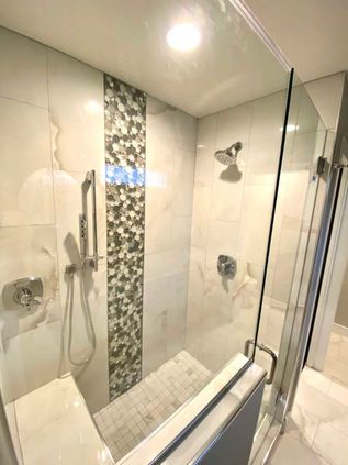 Modern shower with glass door, white tile walls, handheld showerhead, and mosaic accent strip