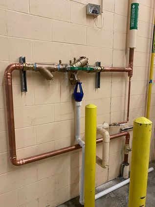 Copper pipes and valves on a beige wall, with yellow bollards in the foreground.