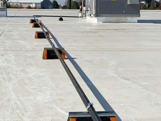 Metal rail on a flat rooftop with orange supports and a ladder-like track leading toward HVAC equipment