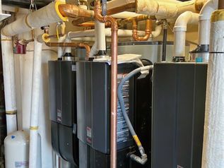 Row of black HVAC units and white pipes in a mechanical room