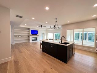 Spacious open-concept kitchen and living room with island, built-in shelves, fireplace, and large windows.