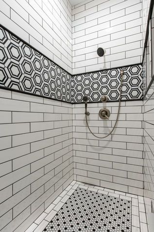 White tiled shower with black geometric accent band and patterned floor, viewed from the corner.