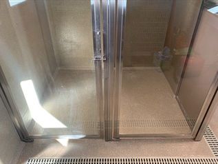 Empty glass elevator interior with stainless steel walls and closed center doors