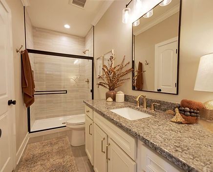 Modern bathroom with granite vanity, large mirror, glass shower, and beige tile walls