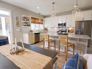 Bright kitchen and dining area with white cabinets, island stools, and a table set in the foreground